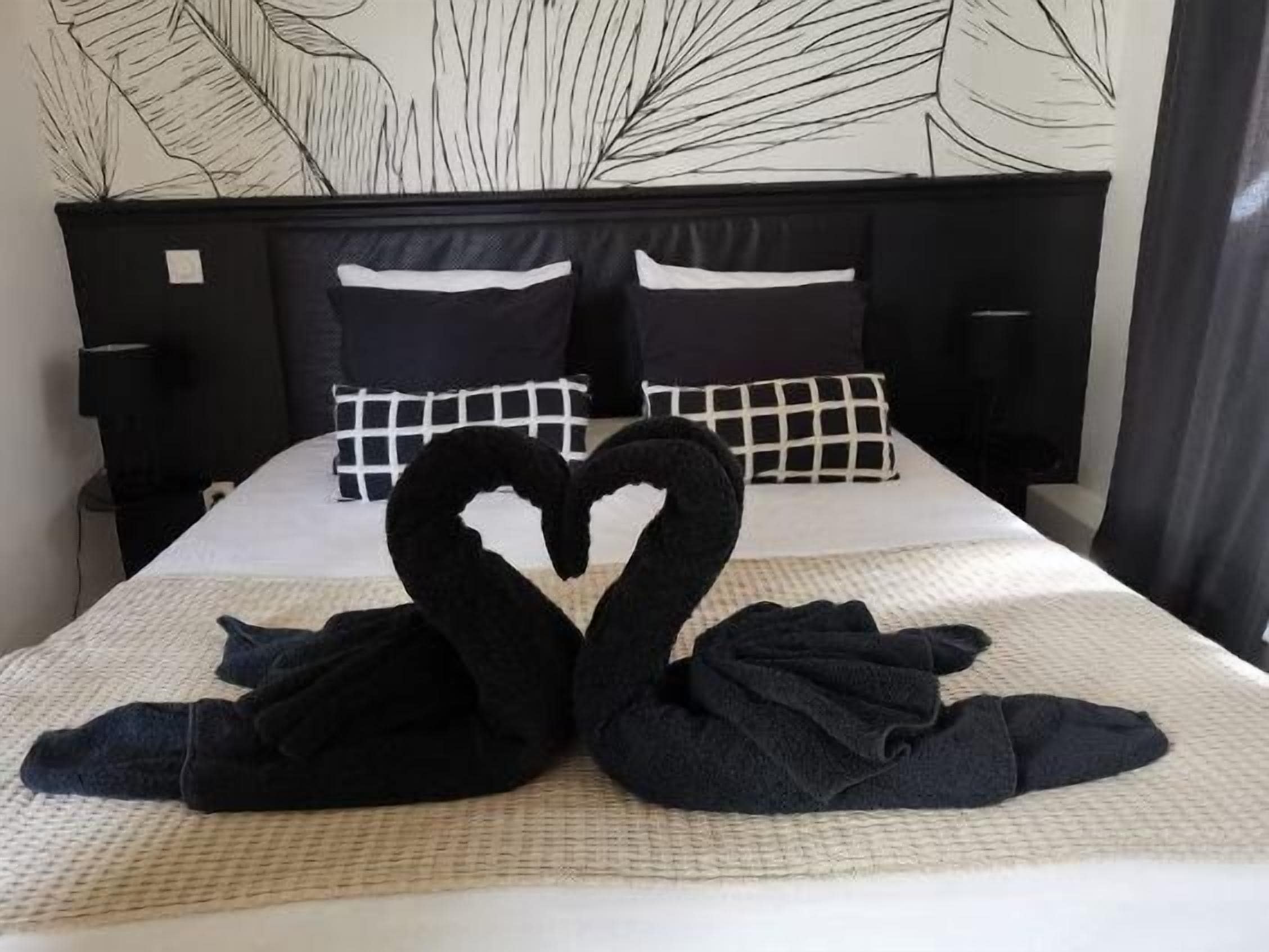 Ein Bett mit einer herzförmigen Handtuchgestaltung, schwarz-weiß karierten Kissen und einer Wand mit einem Blattmuster.