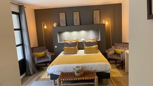 A bedroom with a large bed, two armchairs, a bench, and a wall-mounted light fixture. - Villa Ambrosia (Narbonne)
