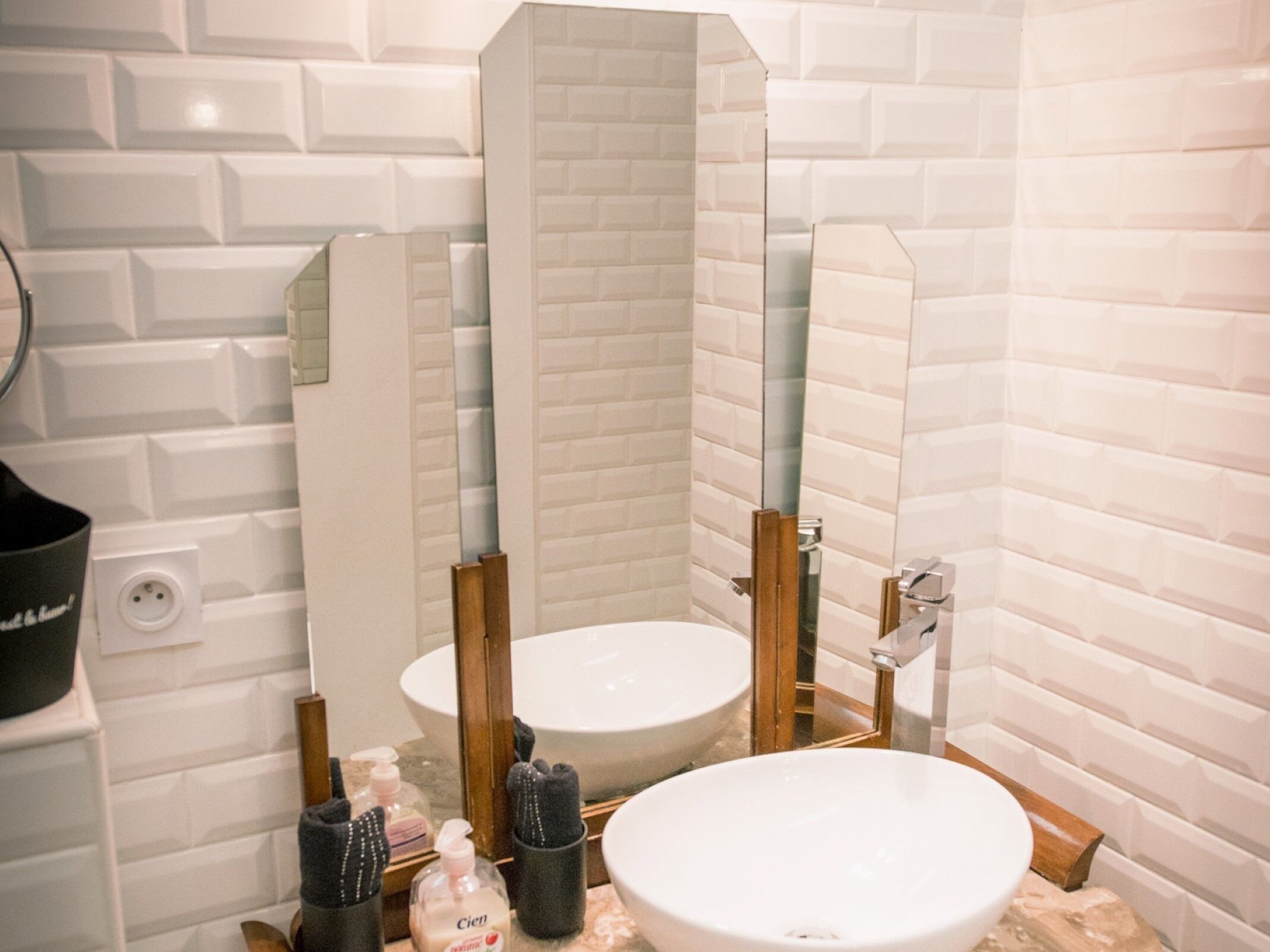 Un bagno con pareti rivestite di piastrelle bianche, un lavandino bianco e uno specchio. Sul mobile ci sono articoli da toilette.