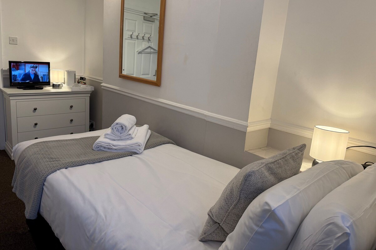 A hotel room with two beds, a TV on a dresser, a mirror, and a lamp.