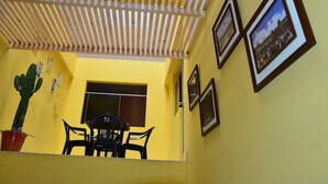 A room with a wooden ceiling, a cactus plant, a dining table with chairs, and framed pictures on the wall. - Tupac Hostel - Lima Airport (Lima)