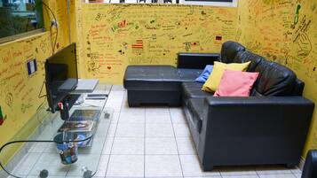 Une pièce avec un canapé en cuir noir, une table basse en verre et un mur jaune recouvert de divers écrits et dessins.