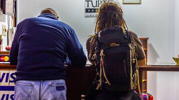 Dos personas frente al mostrador de recepción, con un cartel que dice "TUPTIC HOSTEL" al fondo.