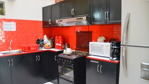 A compact kitchen with black cabinets, a red backsplash, a gas stove, a microwave, and a refrigerator. - Tupac Hostel - Lima Airport (Lima)