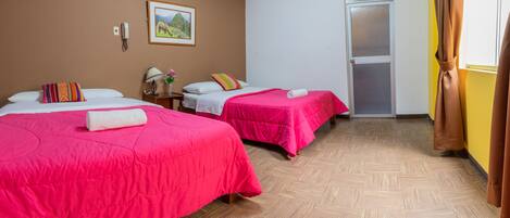 A hotel room with two beds, a wooden floor, a door, and a wall-mounted phone.