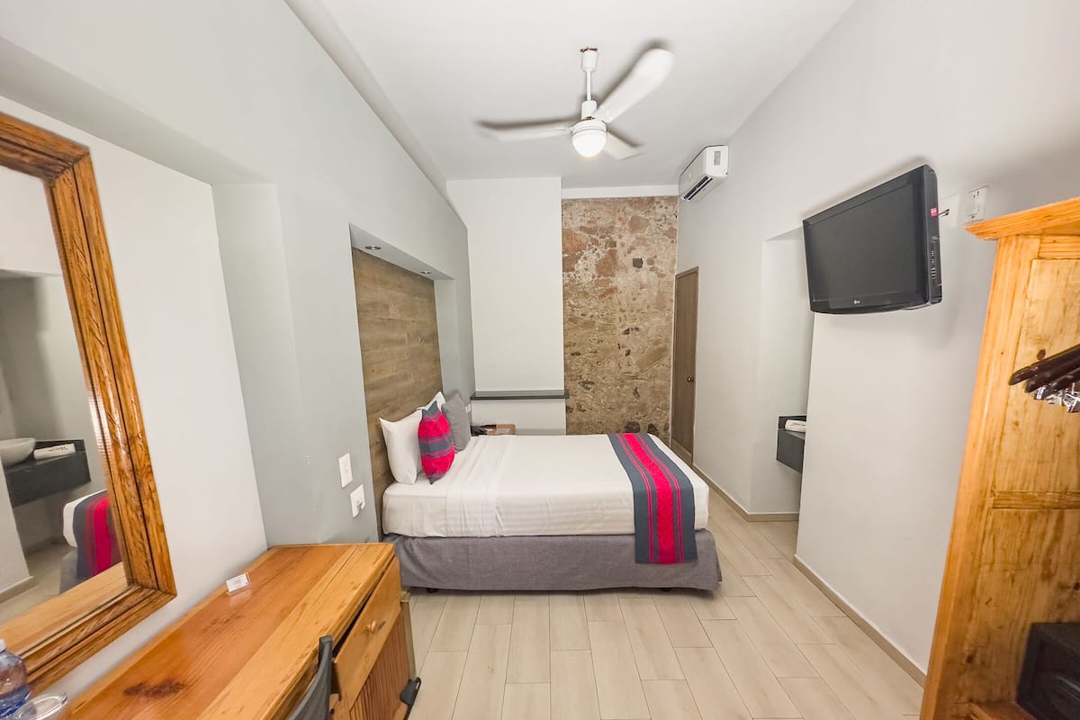 A bedroom with a bed, a wooden dresser, a television, and a ceiling fan.