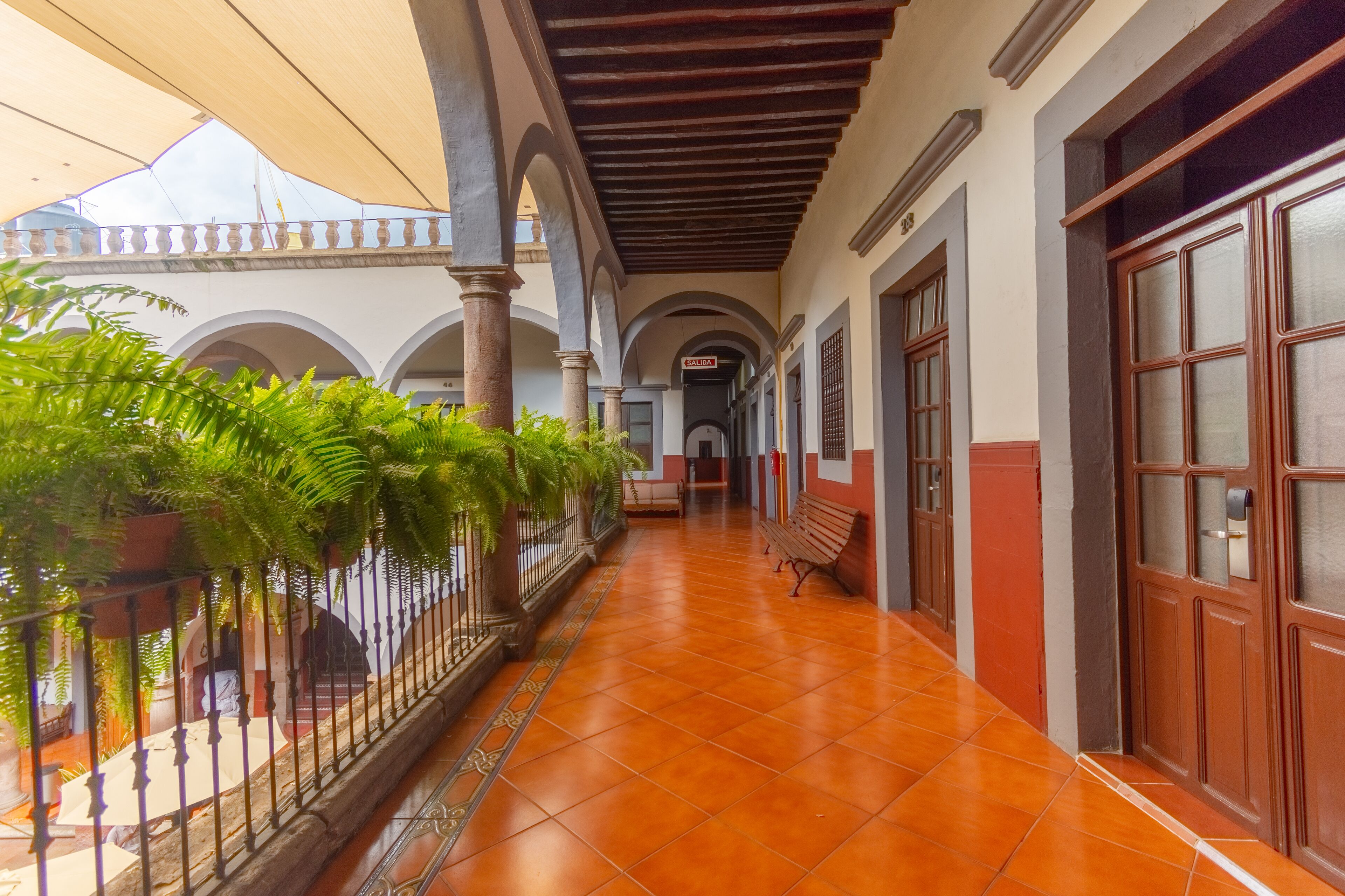 A covered corridor with tiled flooring, benches, and potted plants.