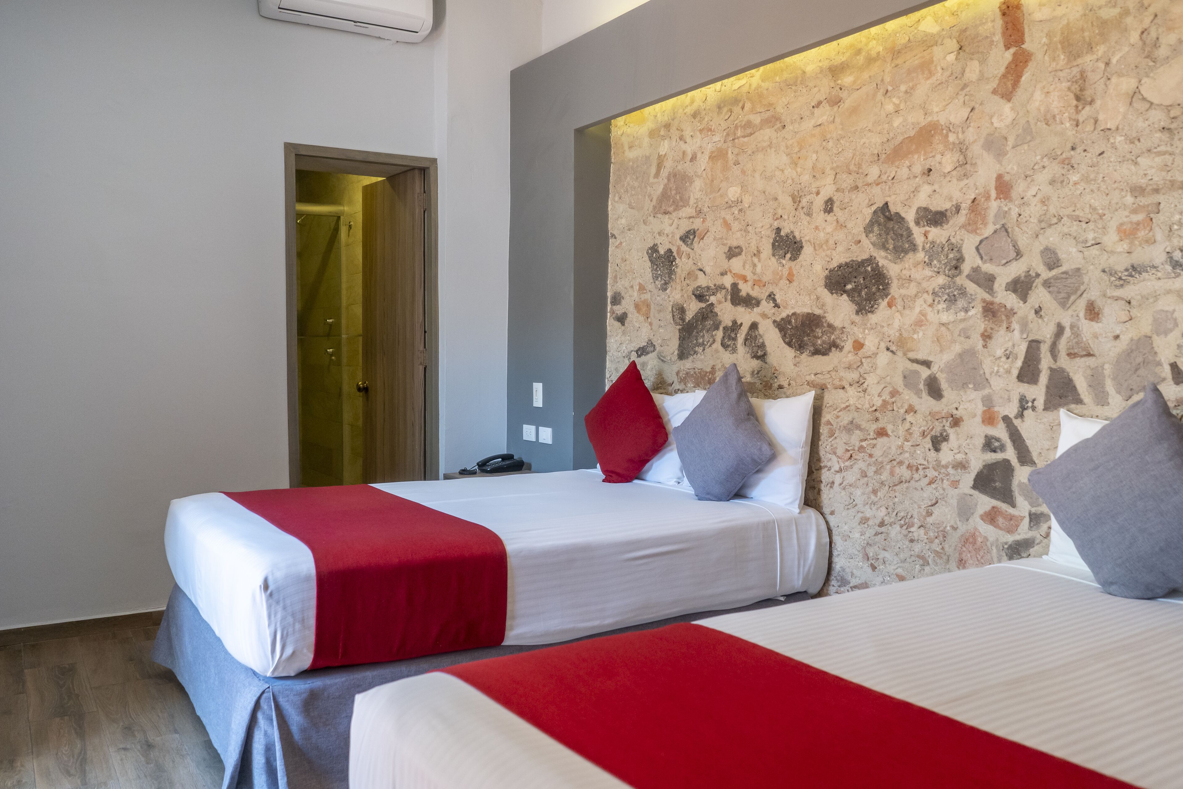 A hotel room with two beds, a stone wall, and a door leading to a bathroom.