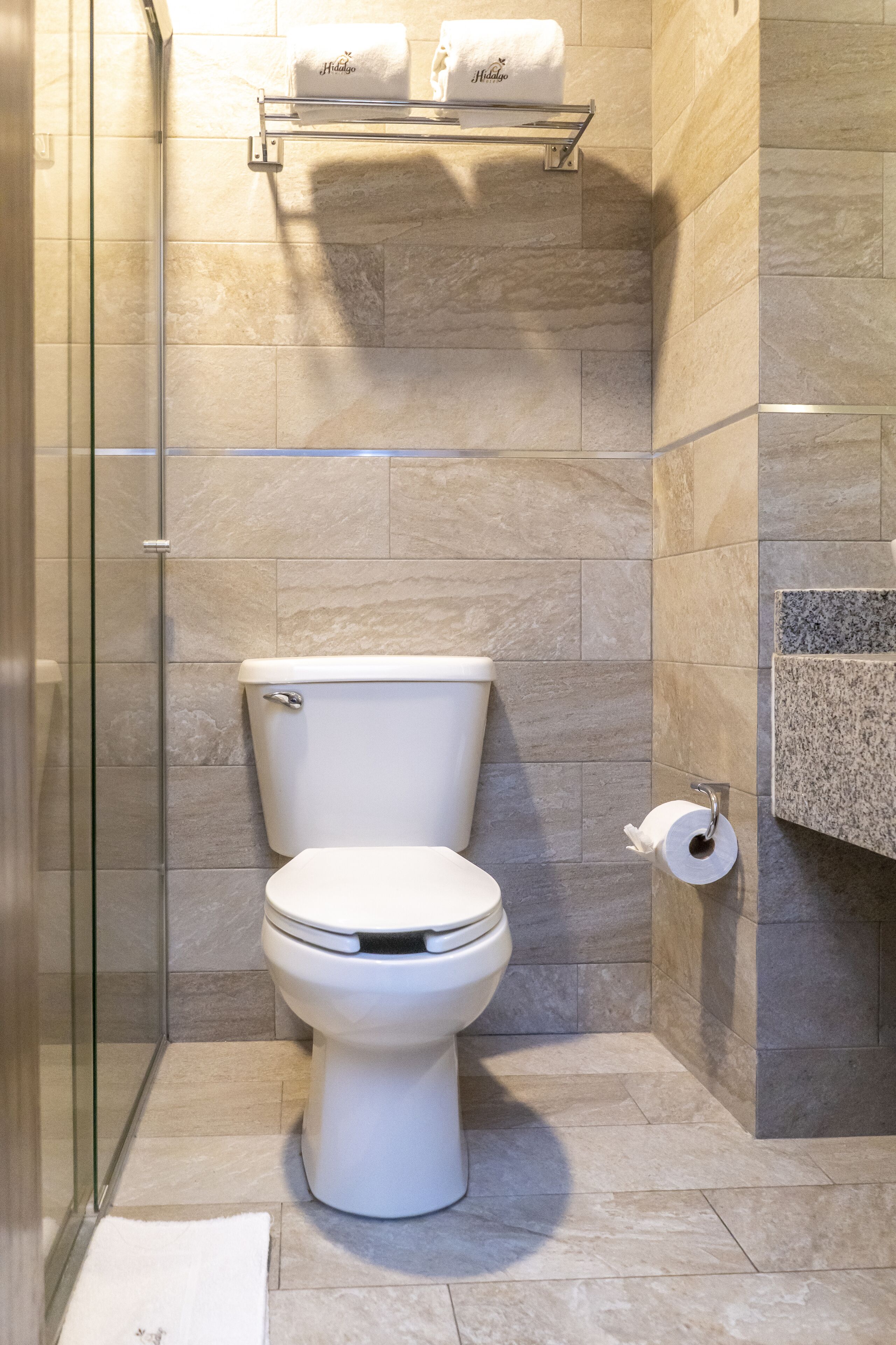 A modern bathroom with a toilet, a glass shower enclosure, and a marble-tiled wall.