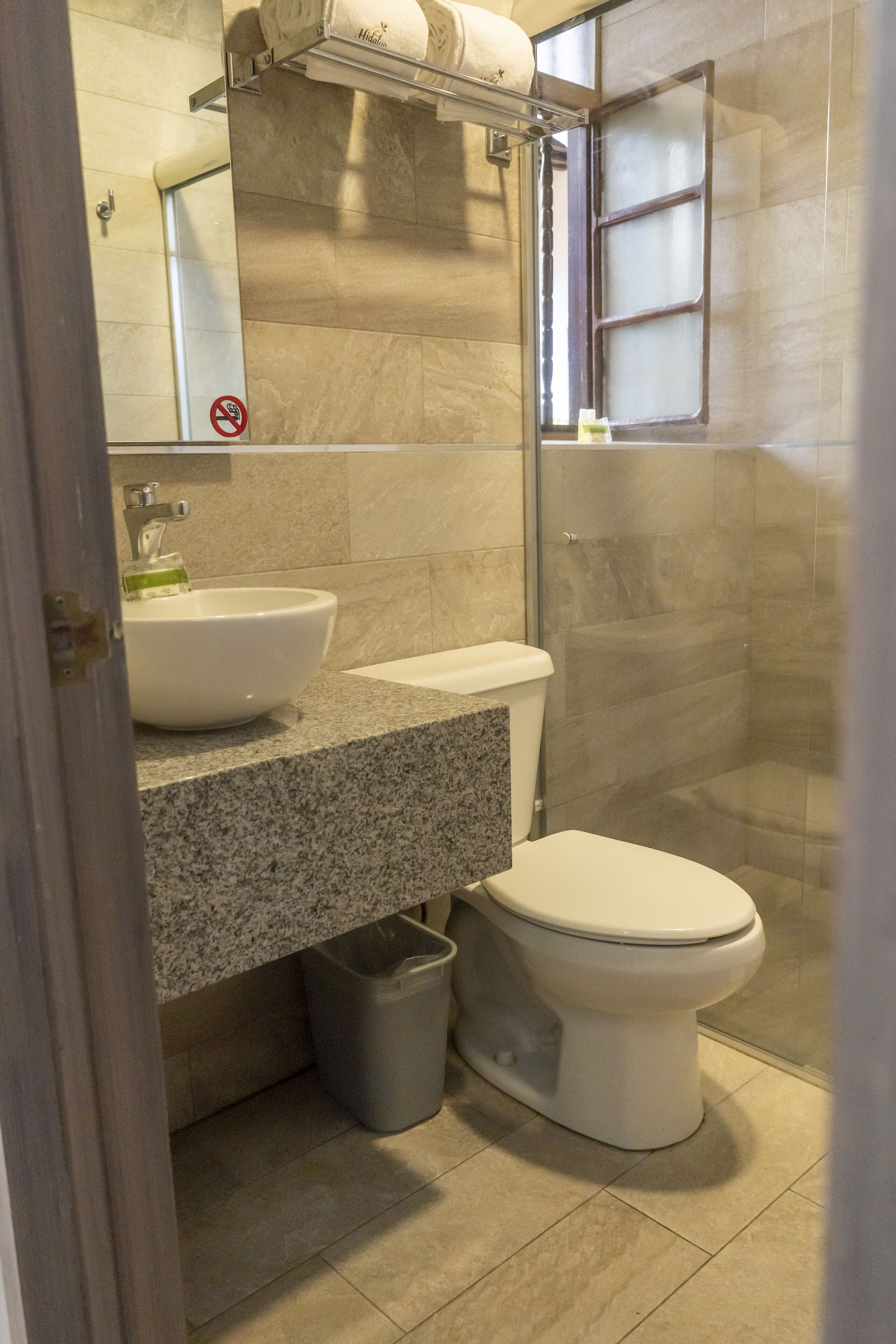 Un baño moderno con encimera de granito, lavamanos blanco, inodoro y mampara de ducha de vidrio.
