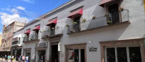Vista de calle con un edificio que presenta balcones con plantas, un letrero que dice 'Lello Restaurant' y un cielo azul despejado.