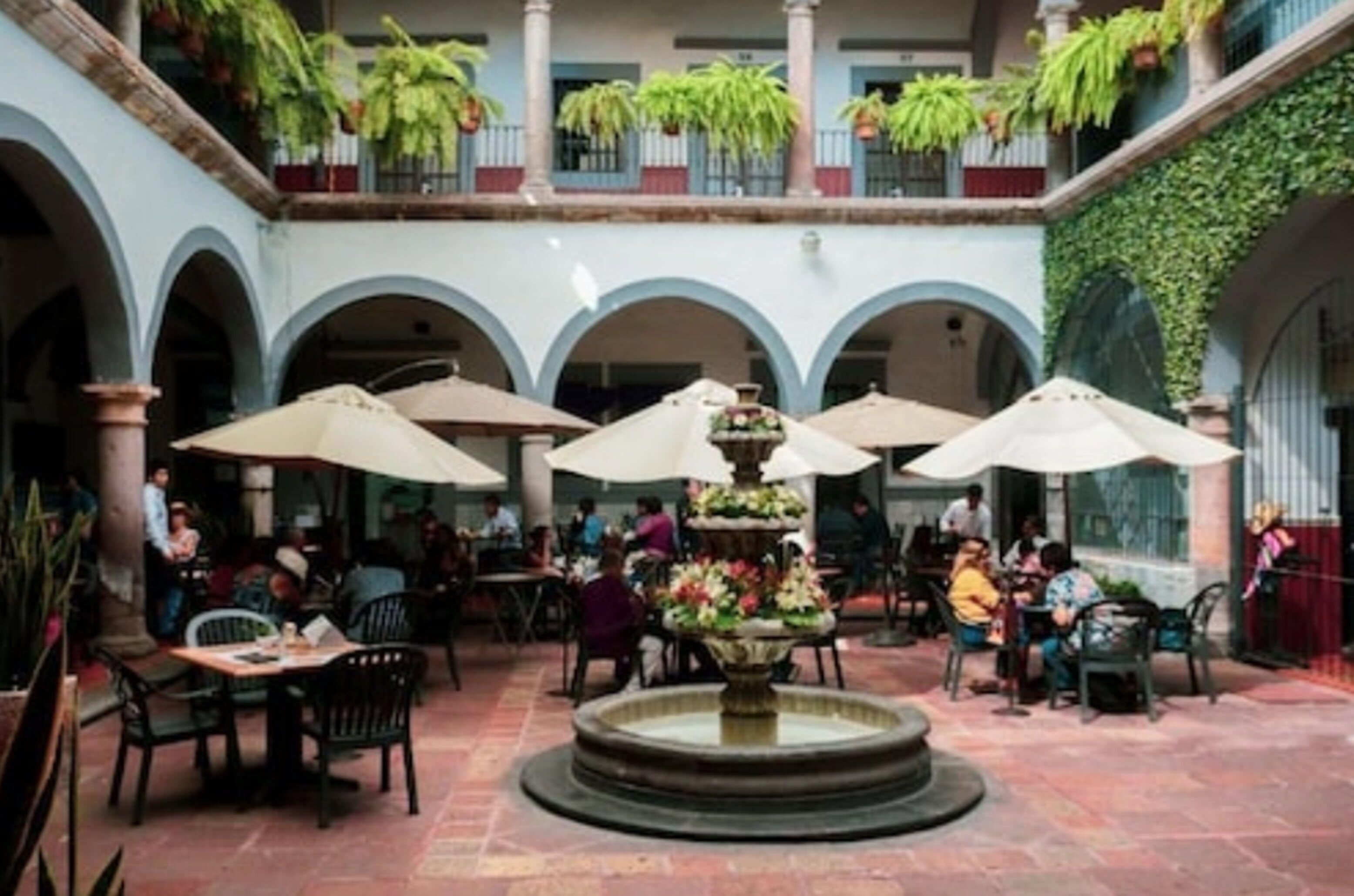 An outdoor courtyard with tables and chairs, a central fountain, and potted plants.