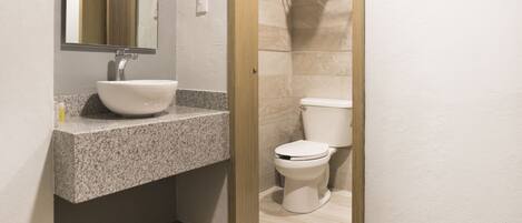 A bathroom with a granite countertop sink, a white toilet, and a shower area with a towel rack.