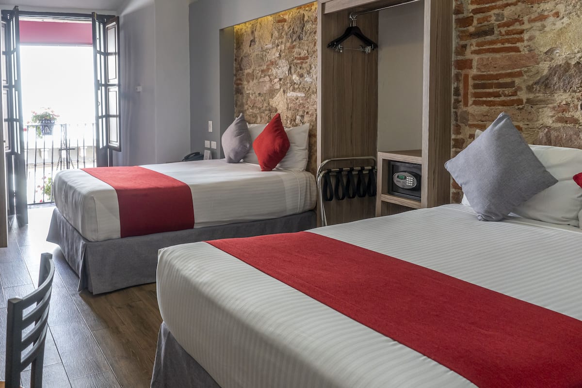 A hotel room with two beds, each with a red and white bedspread, and a brick wall.