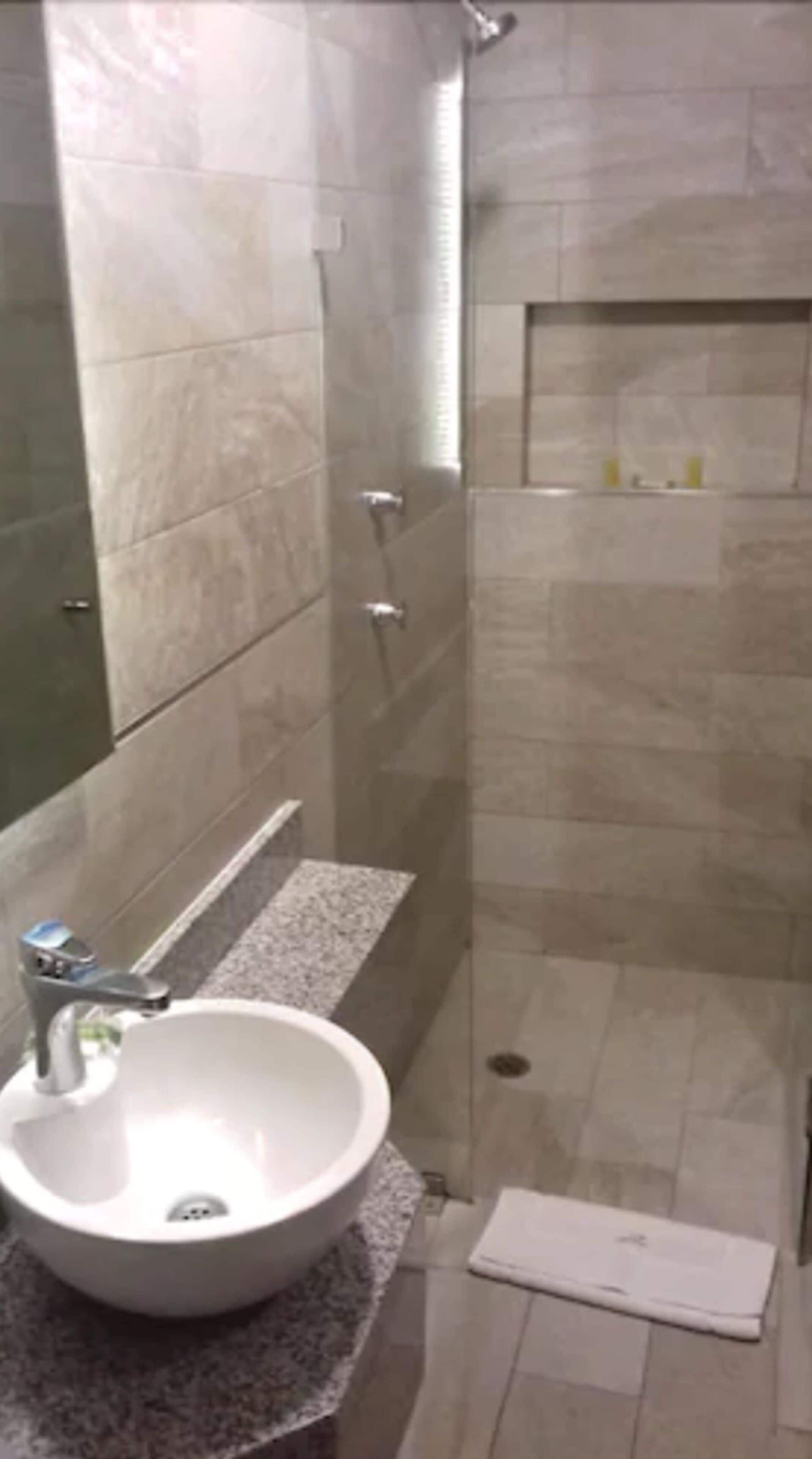 Ein modernes Badezimmer mit einem großen Waschbecken, einer Dusche und einem Spiegel.
