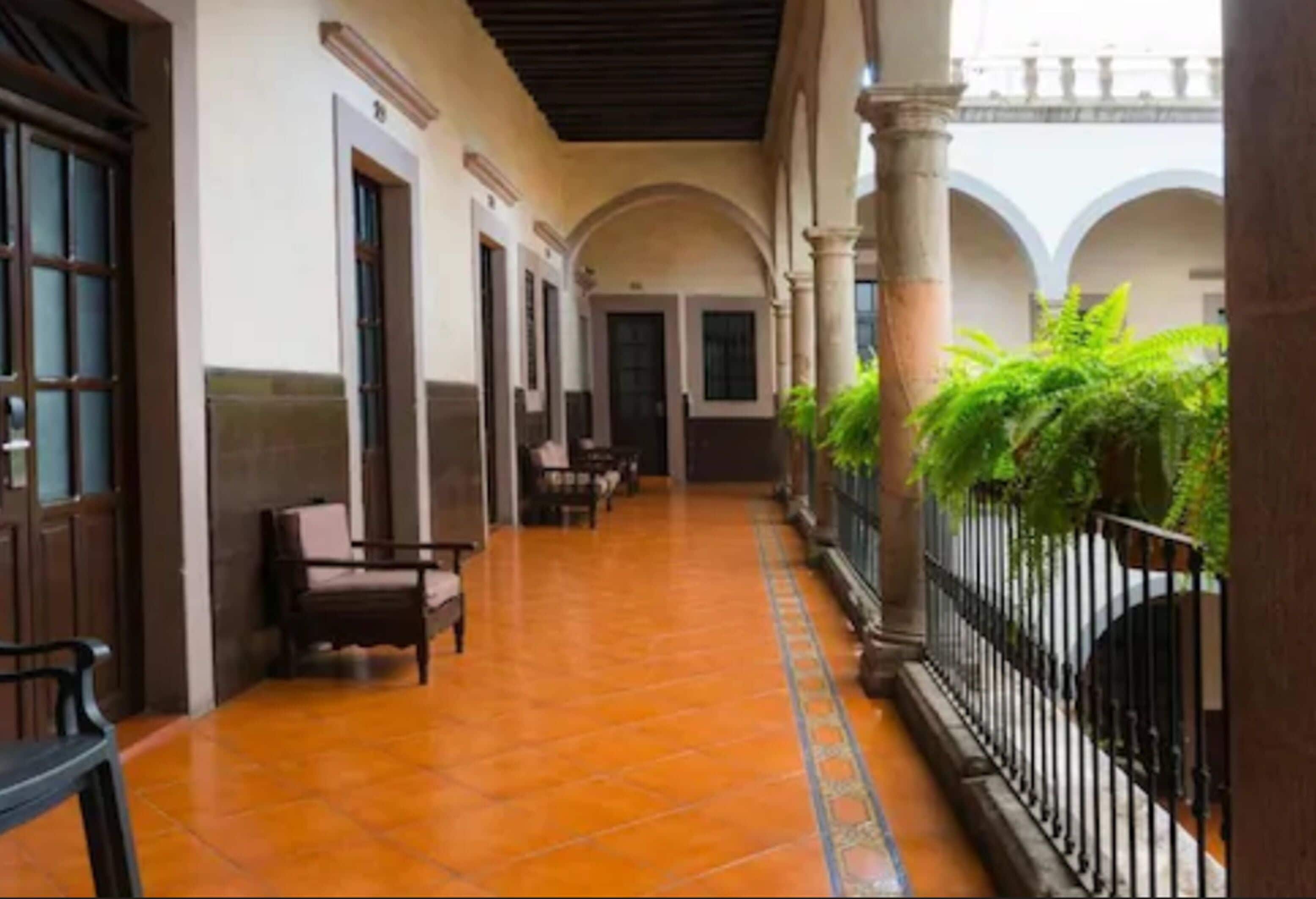 A corridor with tiled flooring, wooden doors, and a railing with greenery.