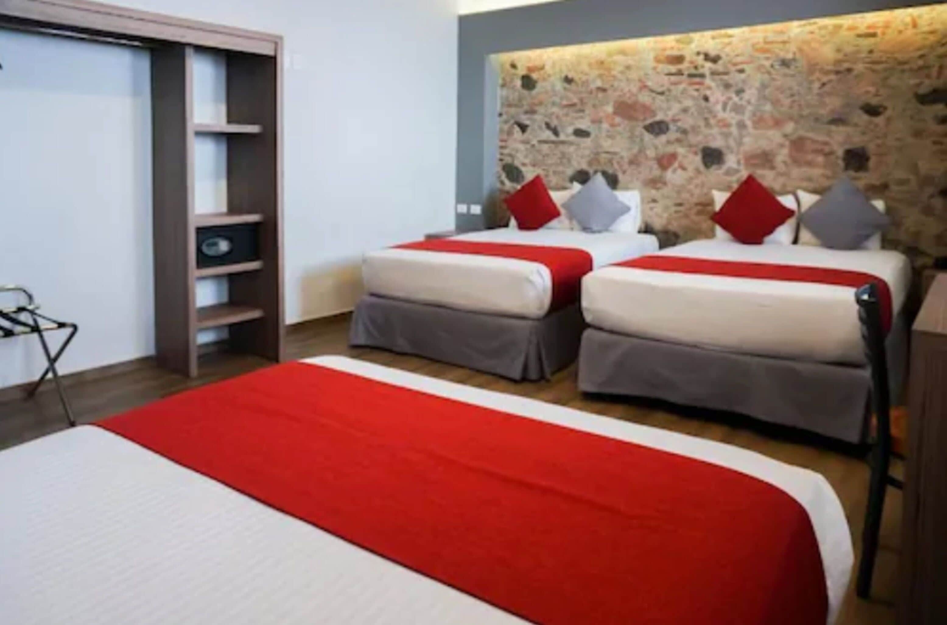 A hotel room with two beds, a red and white bedspread, a stone-patterned headboard, and a wooden wardrobe.