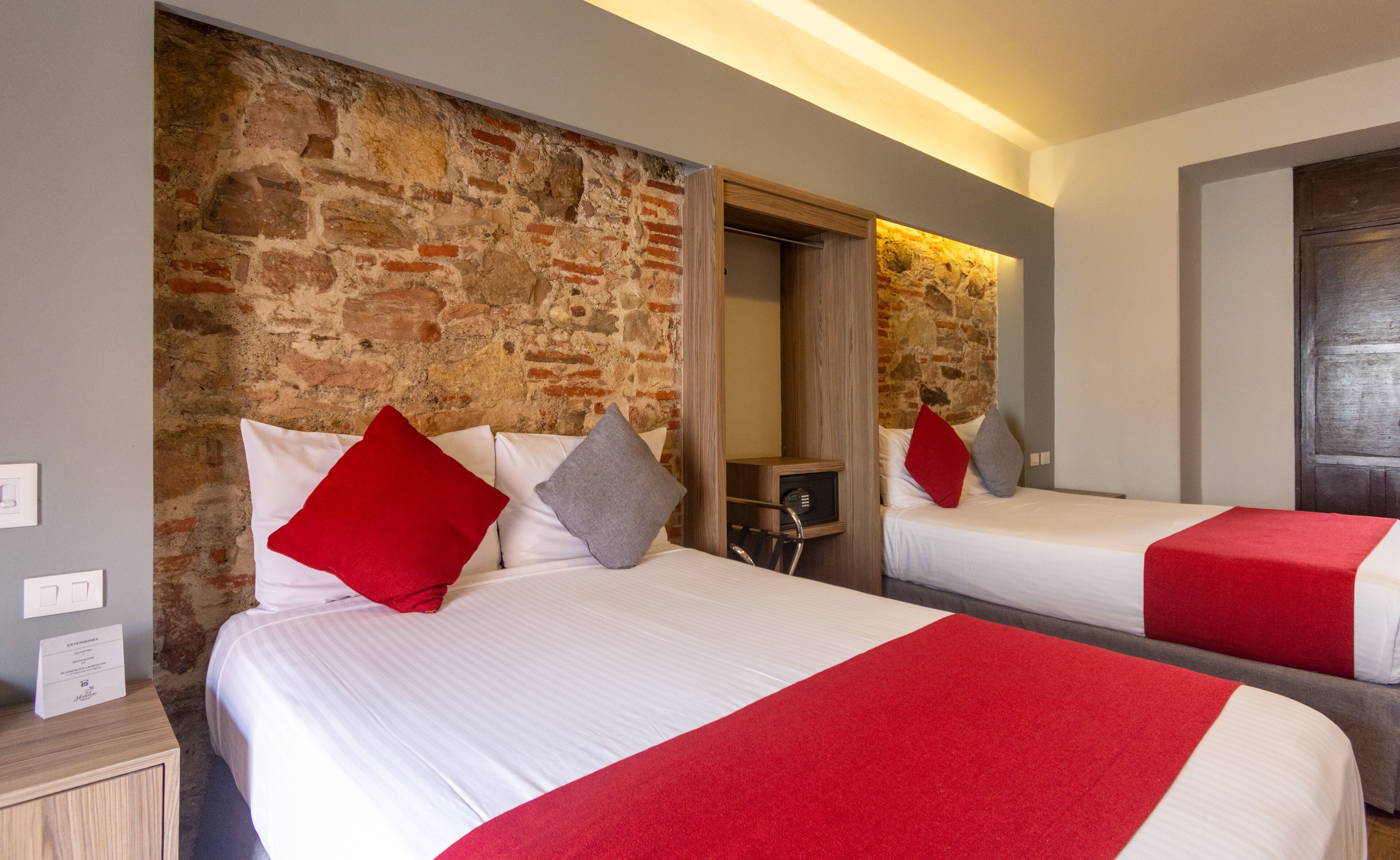Habitación de hotel con dos camas, una pared de piedra y un espejo.