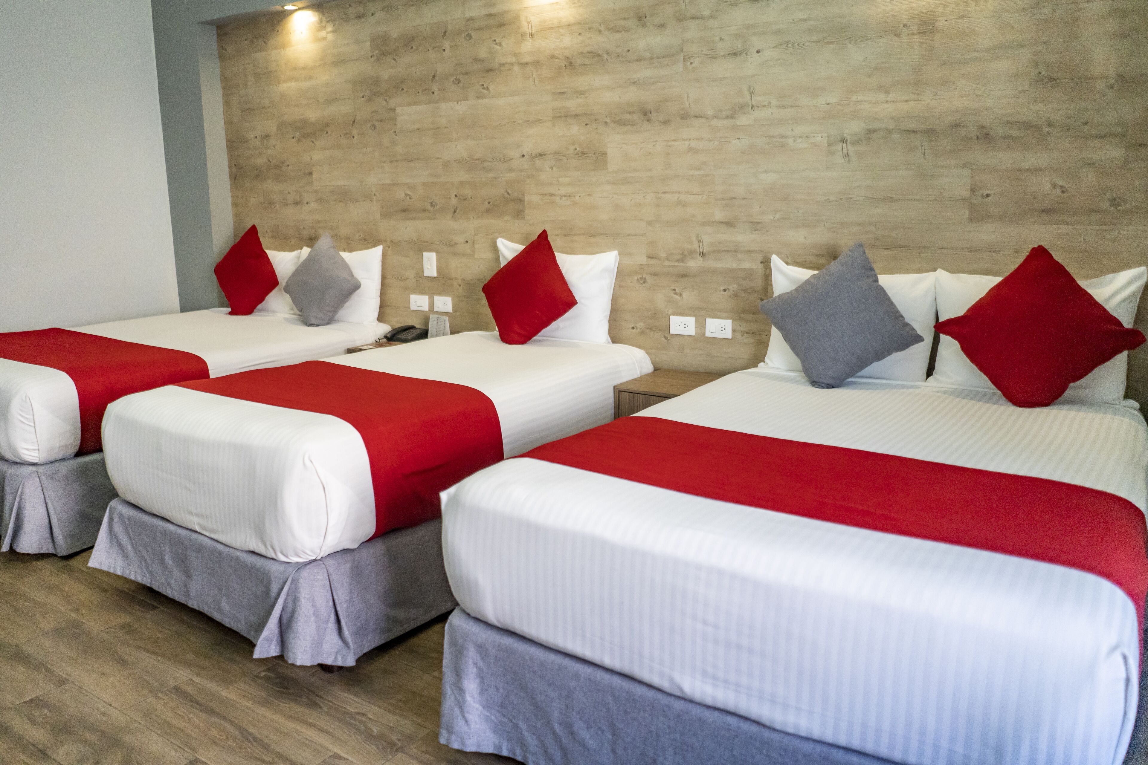 Une chambre d’hôtel avec trois lits, chacun agrémenté de draps blancs et de touches de couleur rouge.