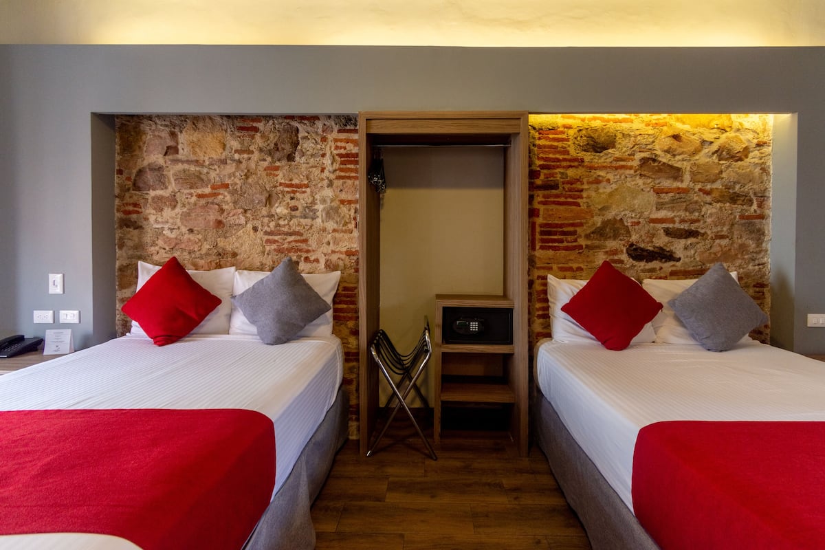 A room with two beds, each with a red and grey pillow, and a brick wall.