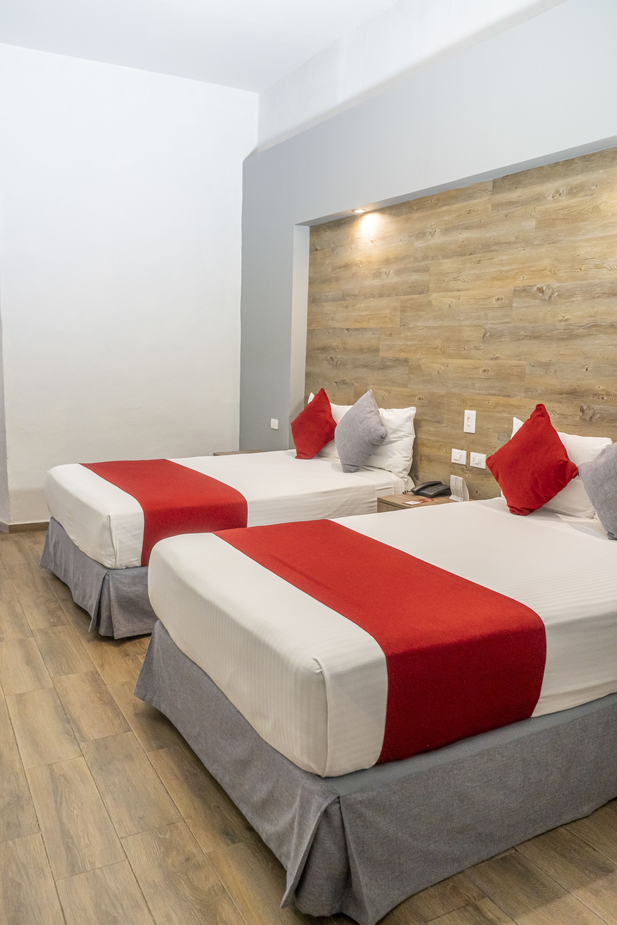 Two single beds with red and grey bedding, a wooden headboard, and a wooden floor.