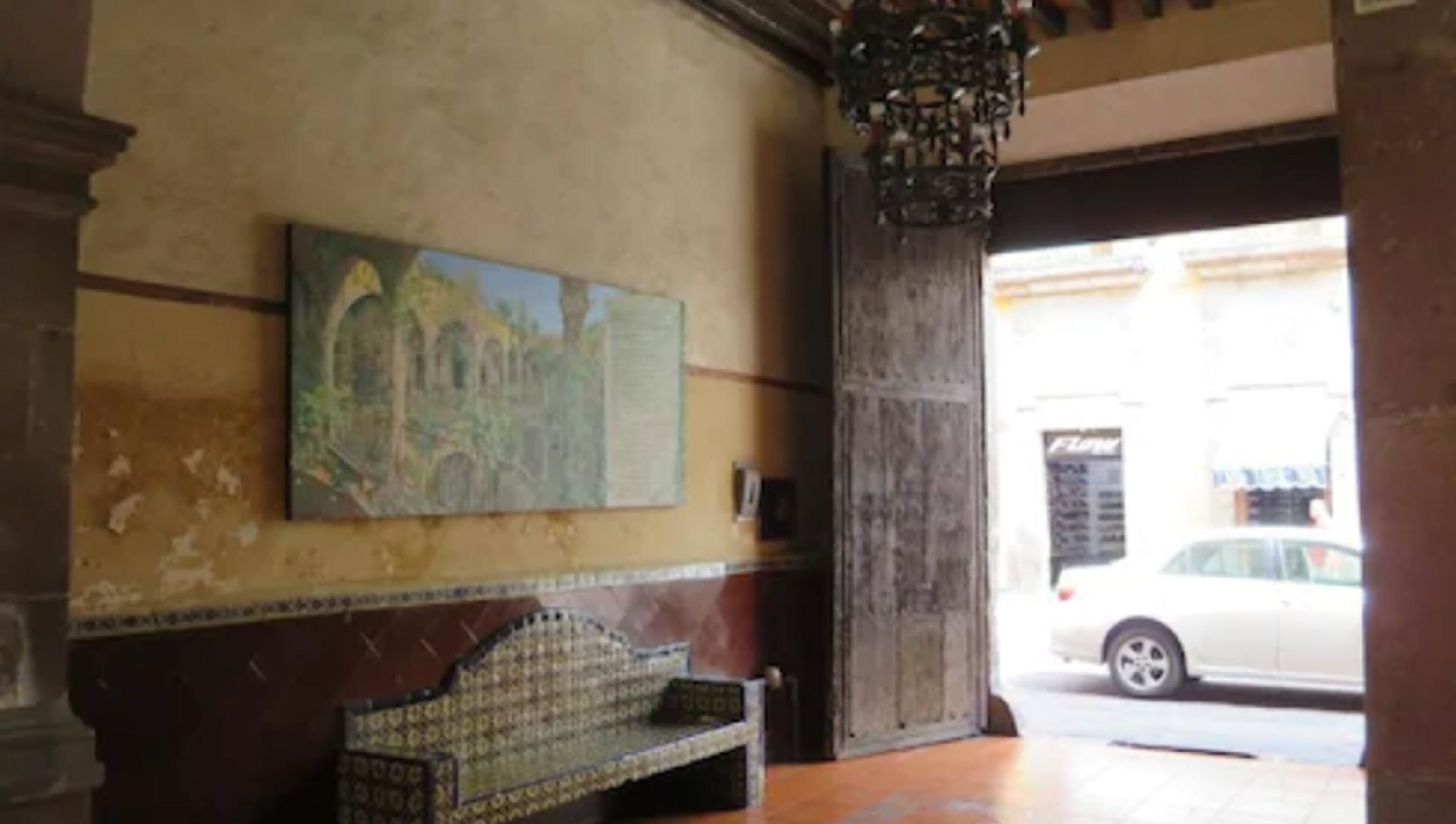 A room with a bench, a painting on the wall, and a view of the street outside.