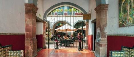 Ein Innenhof mit gefliestem Boden, einer Sitzgruppe in der Mitte und einem Tor zu einem Außenbereich.