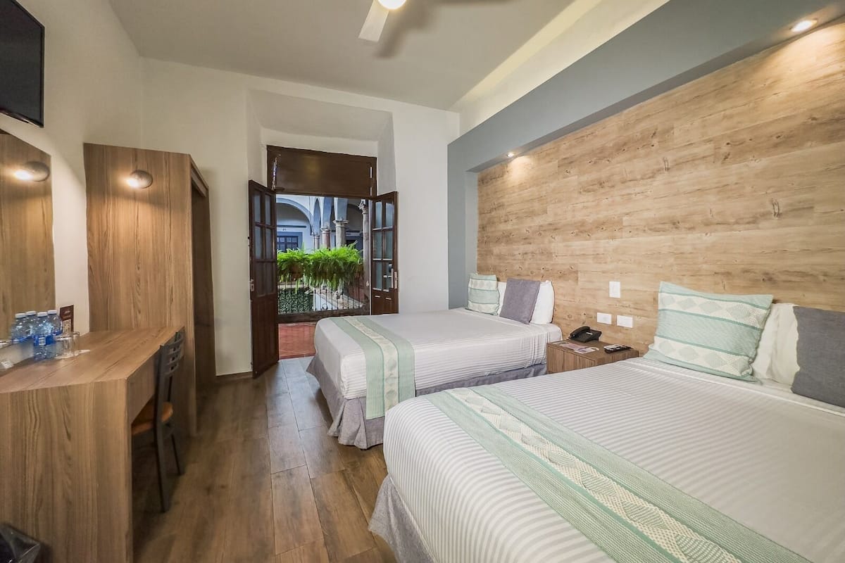 A hotel room with two beds, a desk, and a wooden headboard.