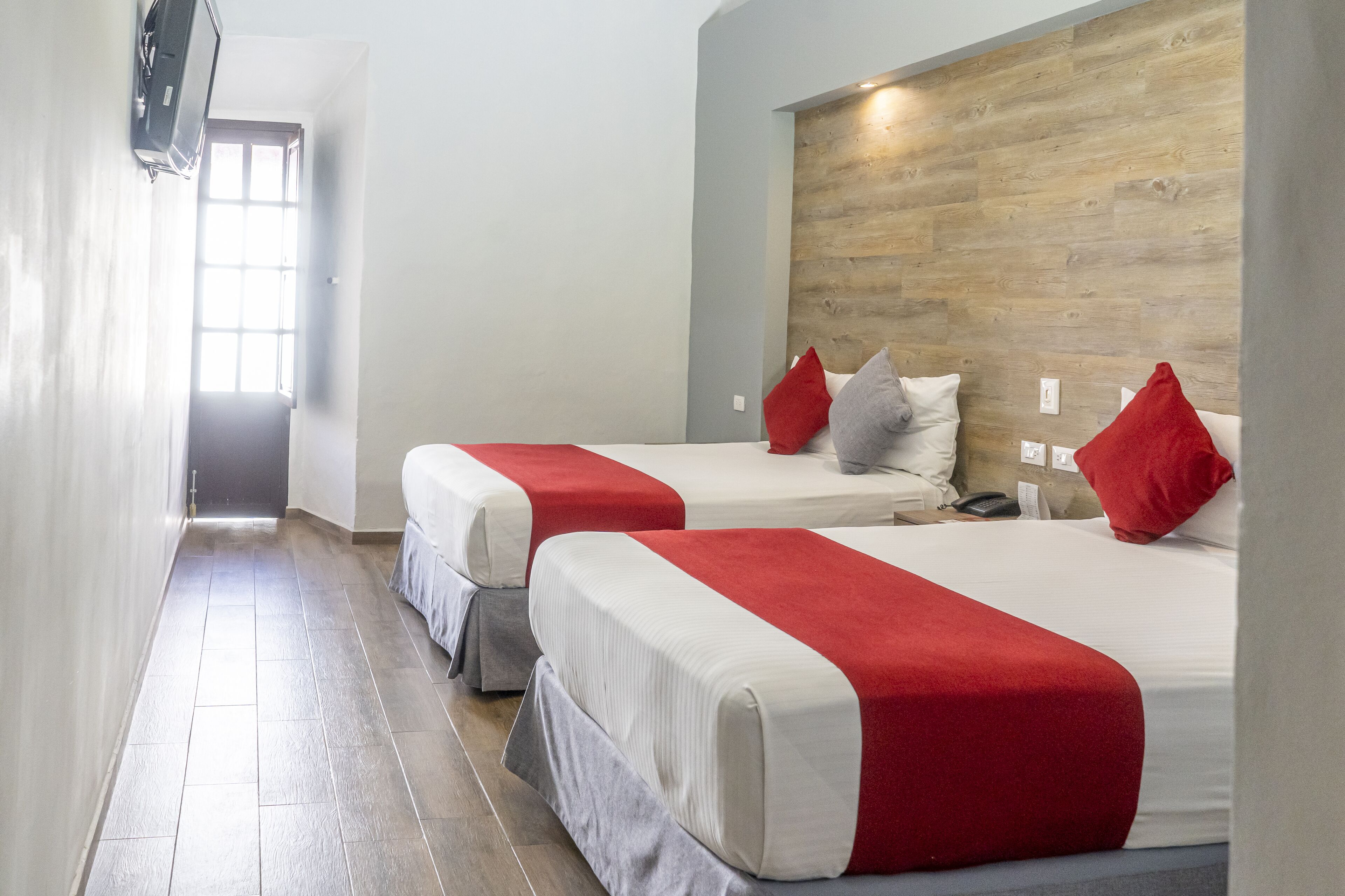 A hotel room with two beds, each with red and white bedding, a wooden headboard, and a small bedside table with a phone.