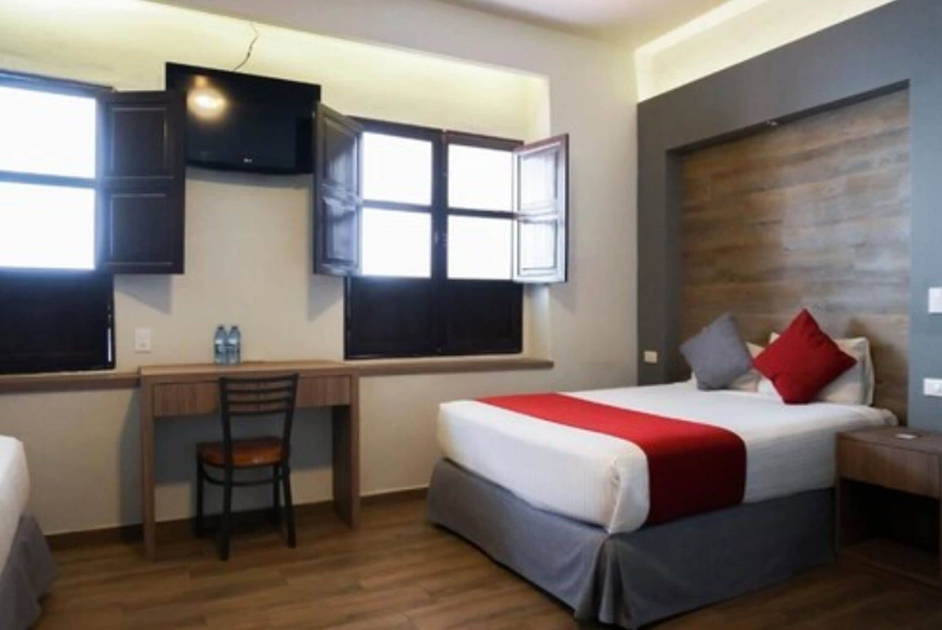 A hotel room with a bed, a desk, a chair, a TV, and a window.