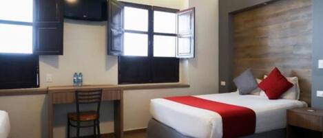A hotel room with a bed, a desk, a chair, a TV, and a window.