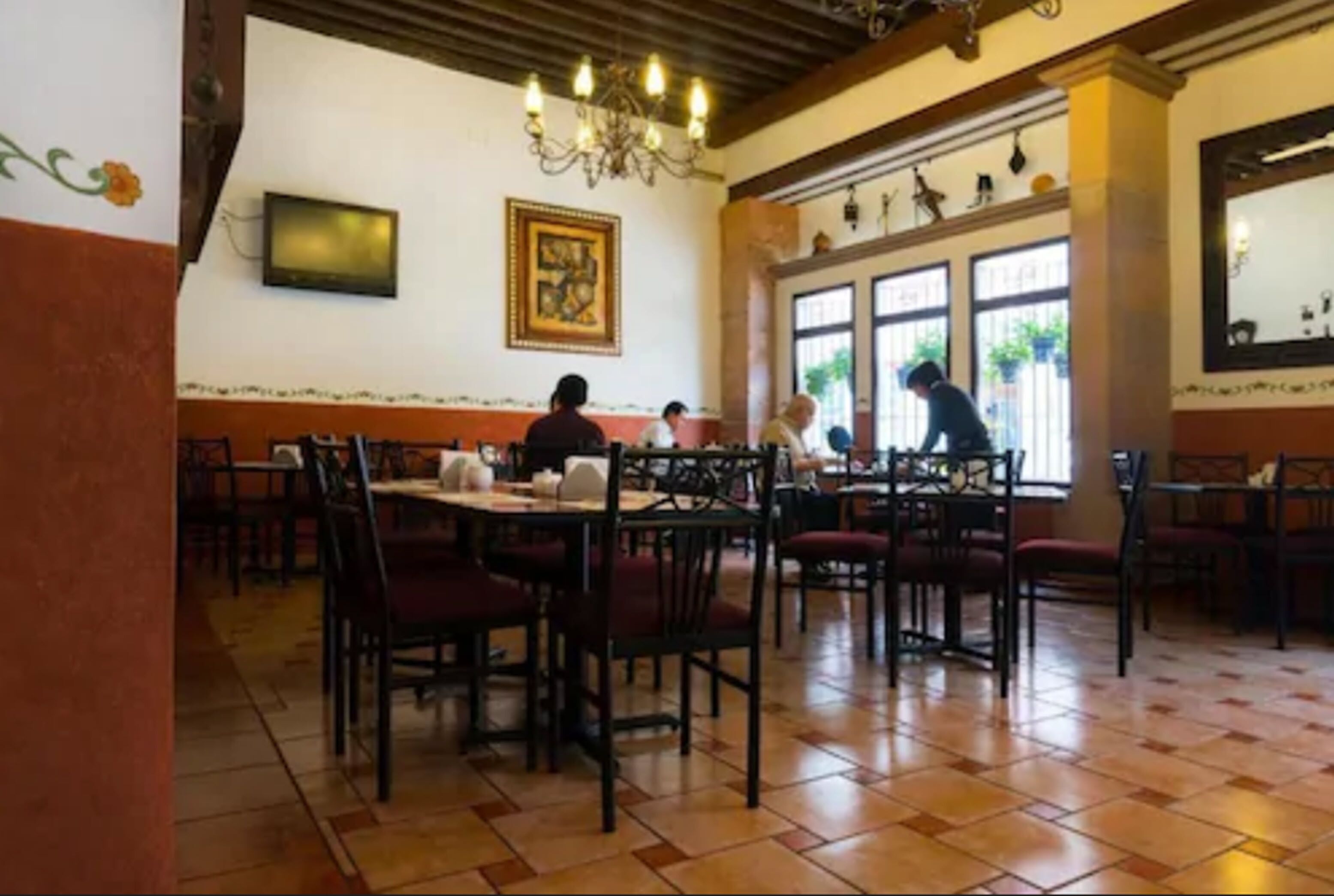 A restaurant with wooden tables and chairs, a chandelier, and large windows.