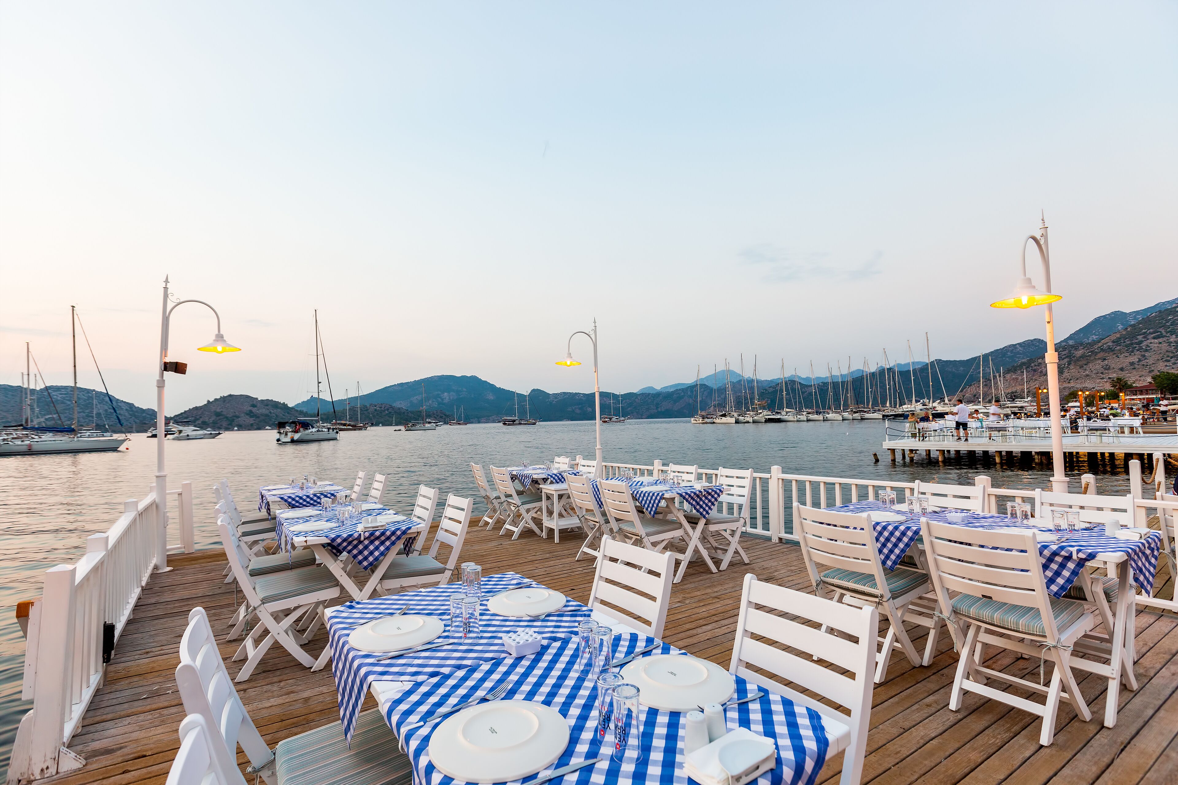 A waterfront restaurant with tables set for dining, overlooking a marina with boats.