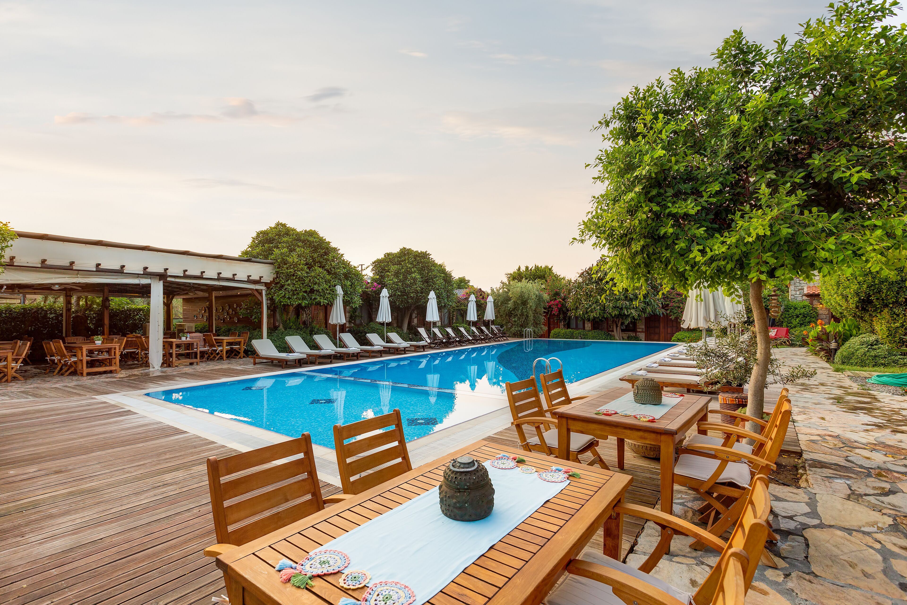 Zona junto a la piscina con terraza de madera, sillas de descanso y un área de estar cubierta.