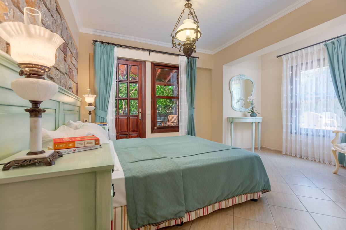 A bedroom with a bed, a nightstand, a lamp, a mirror, and a window with curtains.
