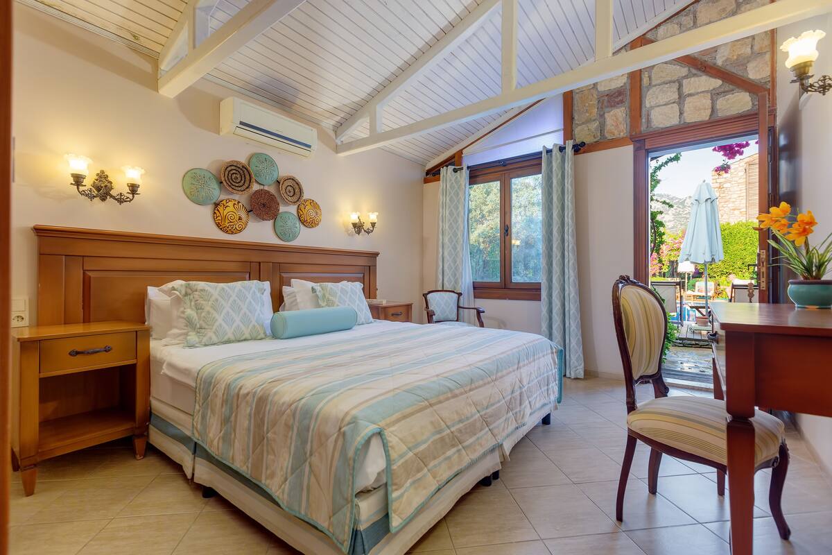 A bedroom with a bed, bedside tables, a chair, a desk, and a view of the outdoors.