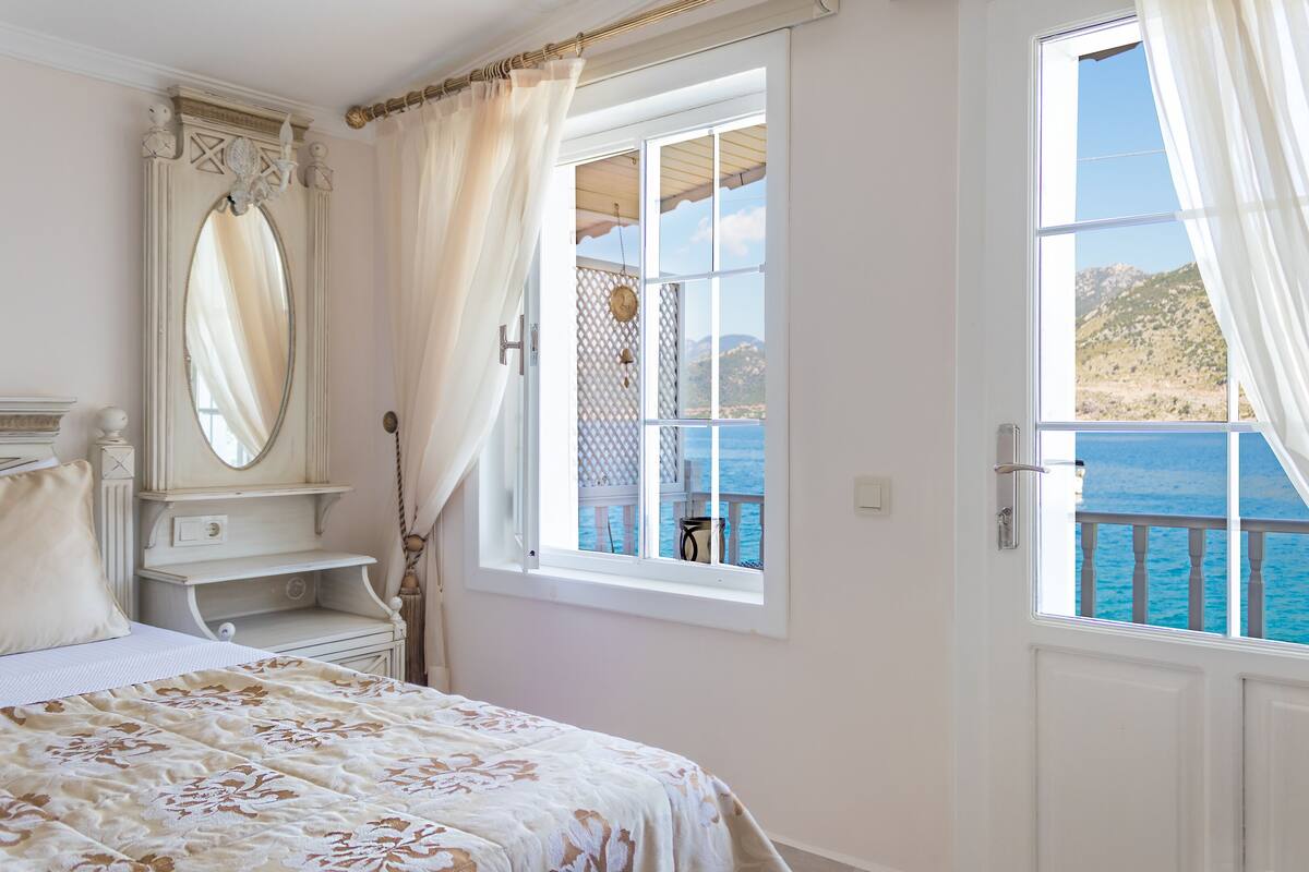 Un dormitorio con cama, cómoda, espejo y ventana con vista al mar.