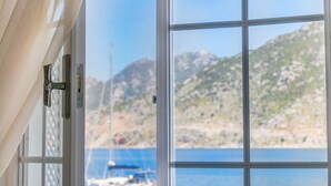 Una ventana con vistas a una zona costera, que incluye un bote y un paisaje montañoso.