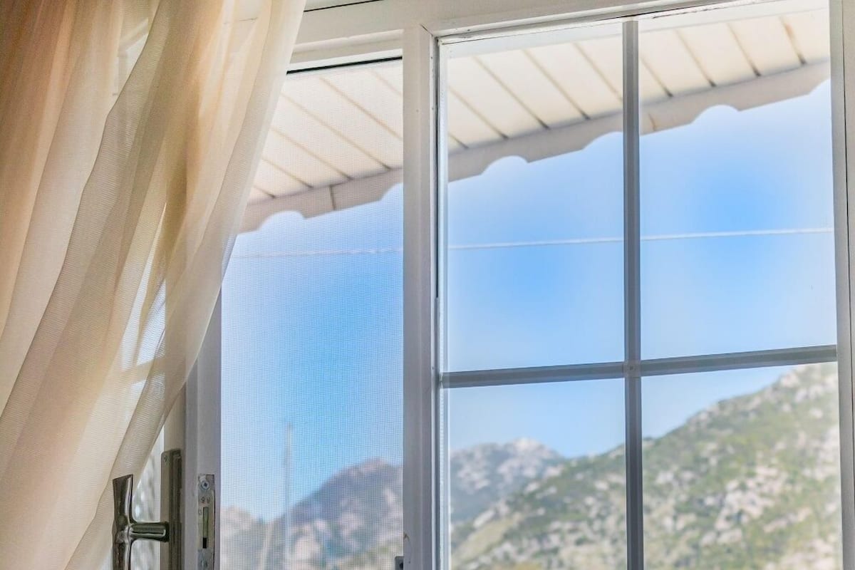 Una ventana con vistas a una zona costera, que incluye un bote y un paisaje montañoso.