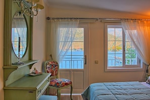 Un dormitorio con cama, cómoda, silla con cojín de colores, espejo y vista hacia una masa de agua a través de una ventana.