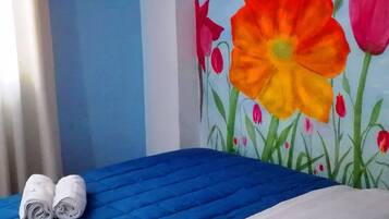 Een hotelkamer met een blauwe sprei, witte kussens en een muurschildering van kleurrijke bloemen.