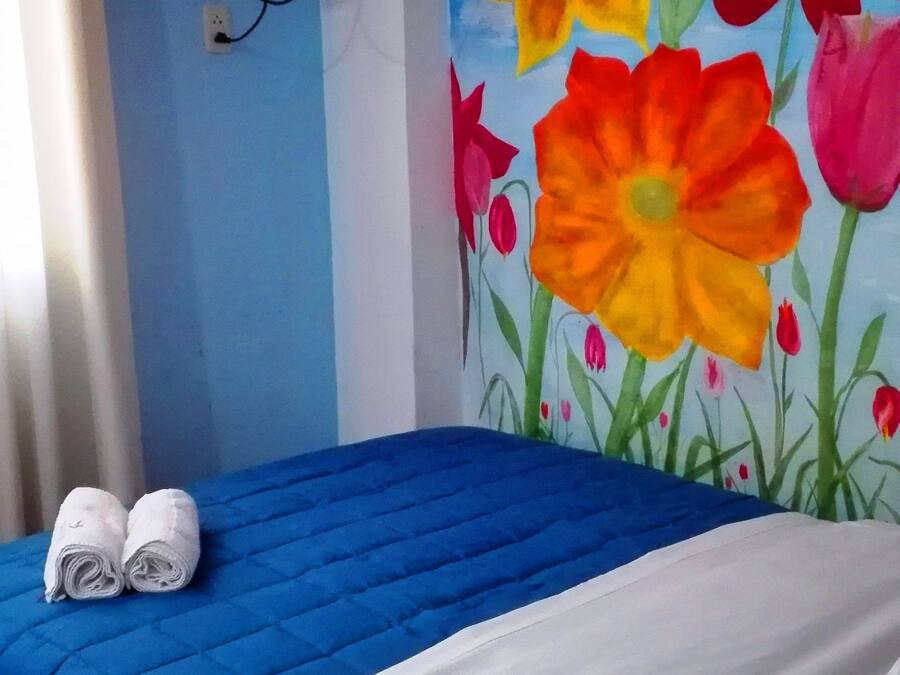 Een hotelkamer met een blauwe sprei, witte kussens en een muurschildering van kleurrijke bloemen.