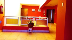 Un hall d’hôtel avec un mur rouge, un comptoir d’accueil, un extincteur et une plante en pot.