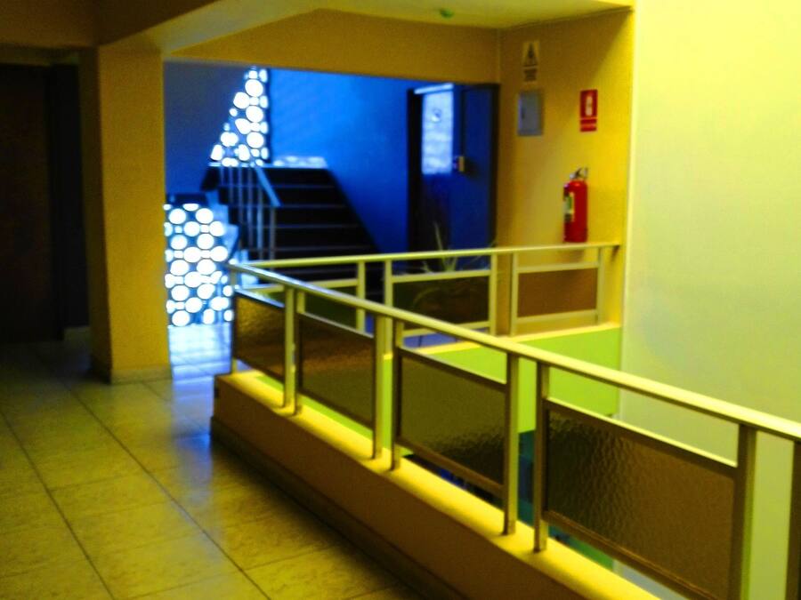 Un pasillo con barandilla, una escalera y un extintor en la pared.