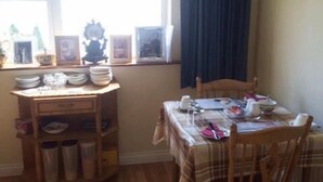 A dining area with a wooden table and chairs, a window with curtains, and a shelf with plates and bowls. - Clooniff House (Galway)