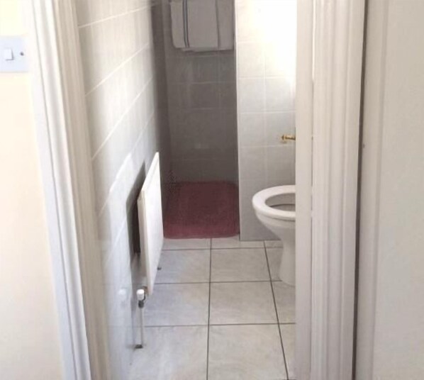 A narrow bathroom with a toilet, a radiator, and a tiled floor.