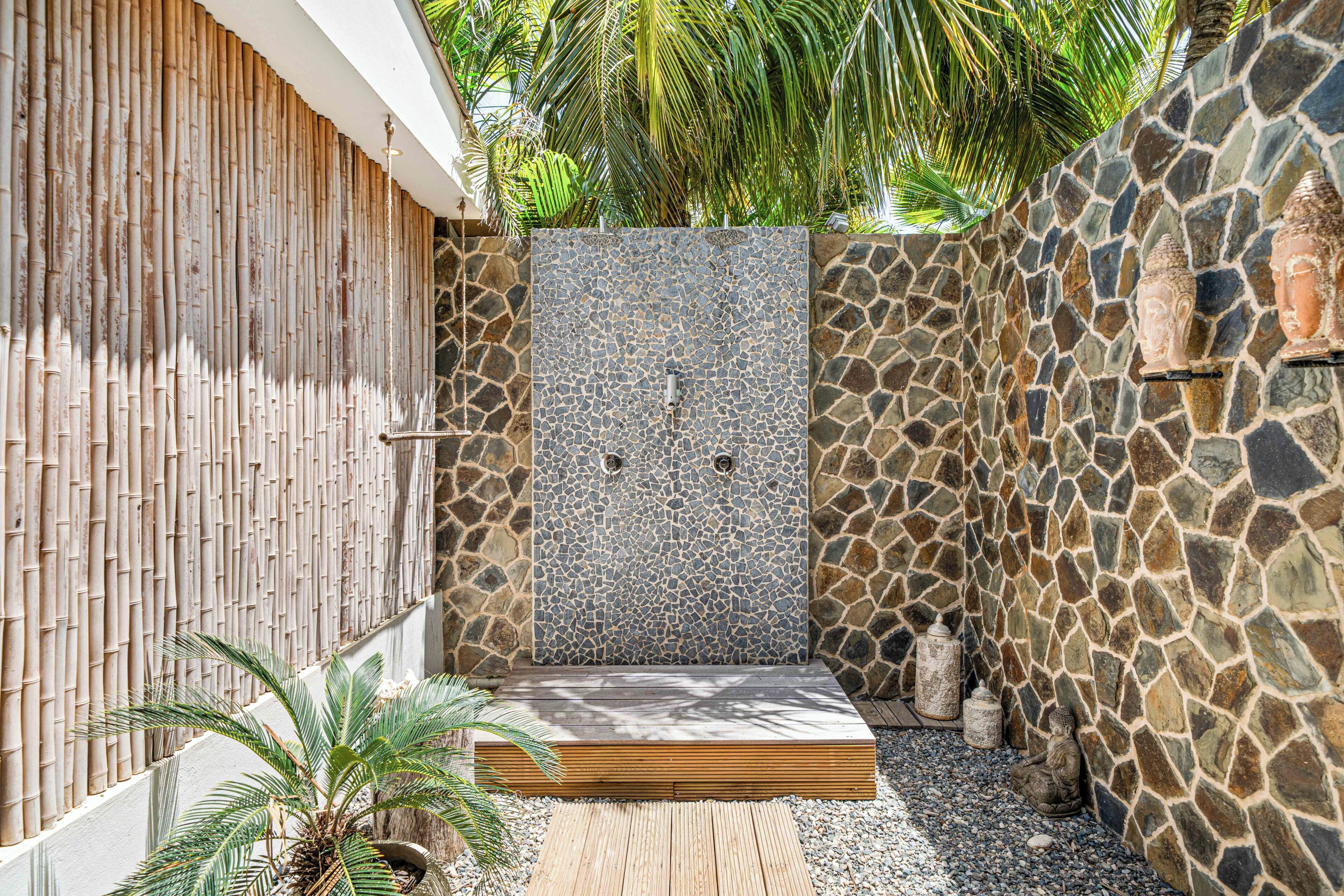 A private outdoor shower area with a stone wall, bamboo fence, and a wooden platform.