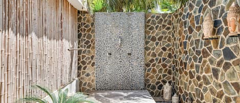 A private outdoor shower area with a stone wall, bamboo fence, and a wooden platform.