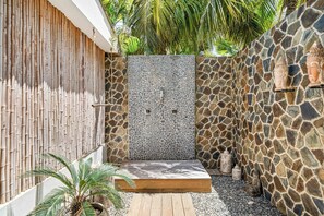 Un espace de douche extérieur privatif, agrémenté d’un mur en pierre, d’une clôture en bambou et d’une plateforme en bois.