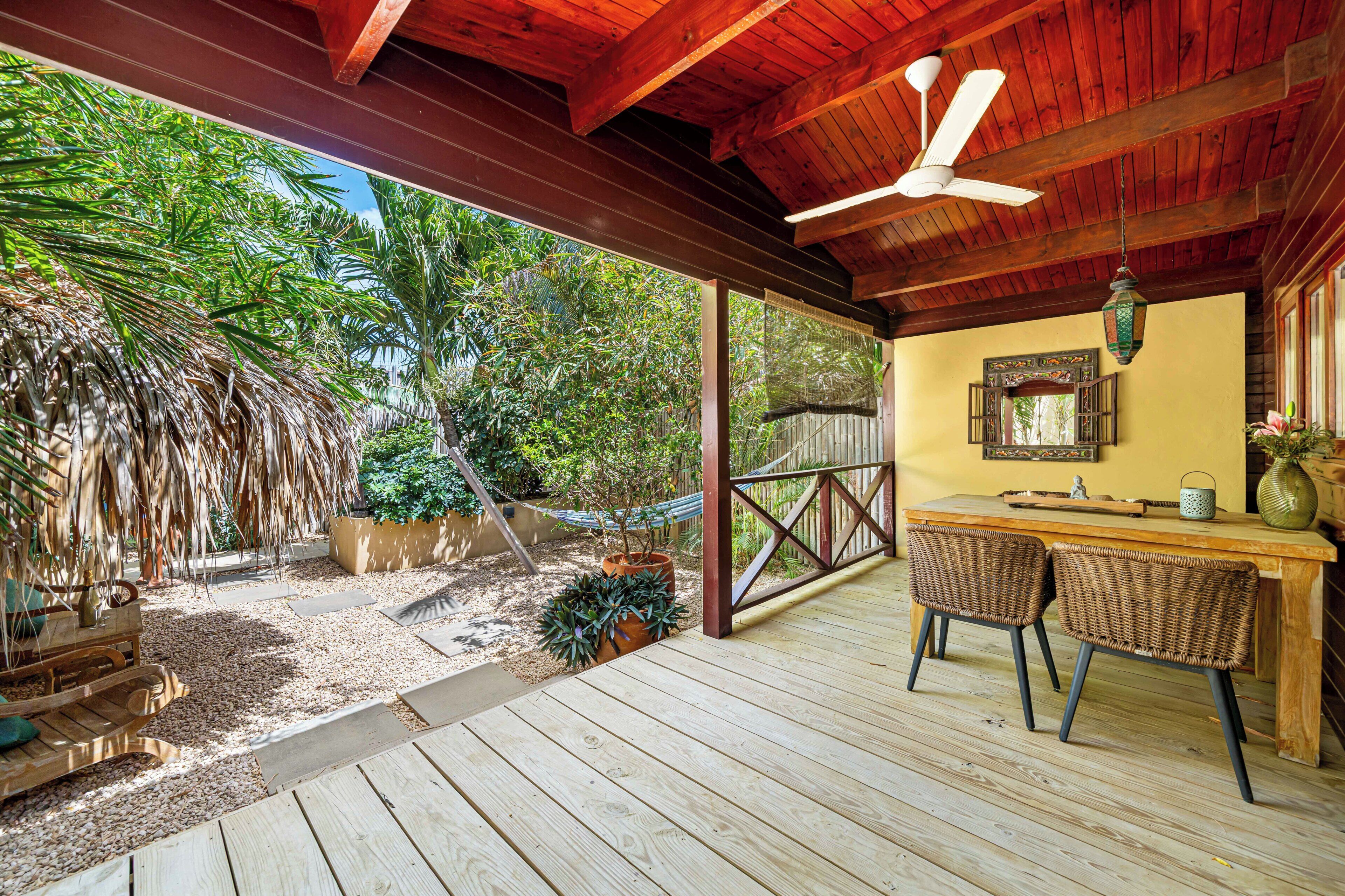 A wooden deck with a ceiling fan, wicker chairs, a wooden table, and a hammock.